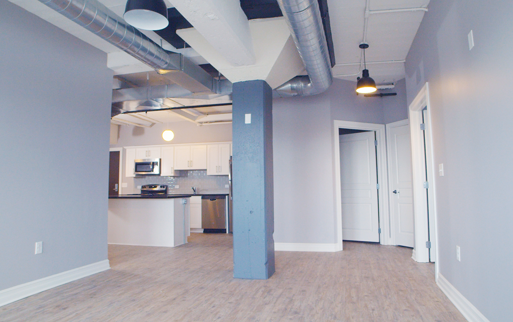 an empty living room with a blue pillar and a kitchen
