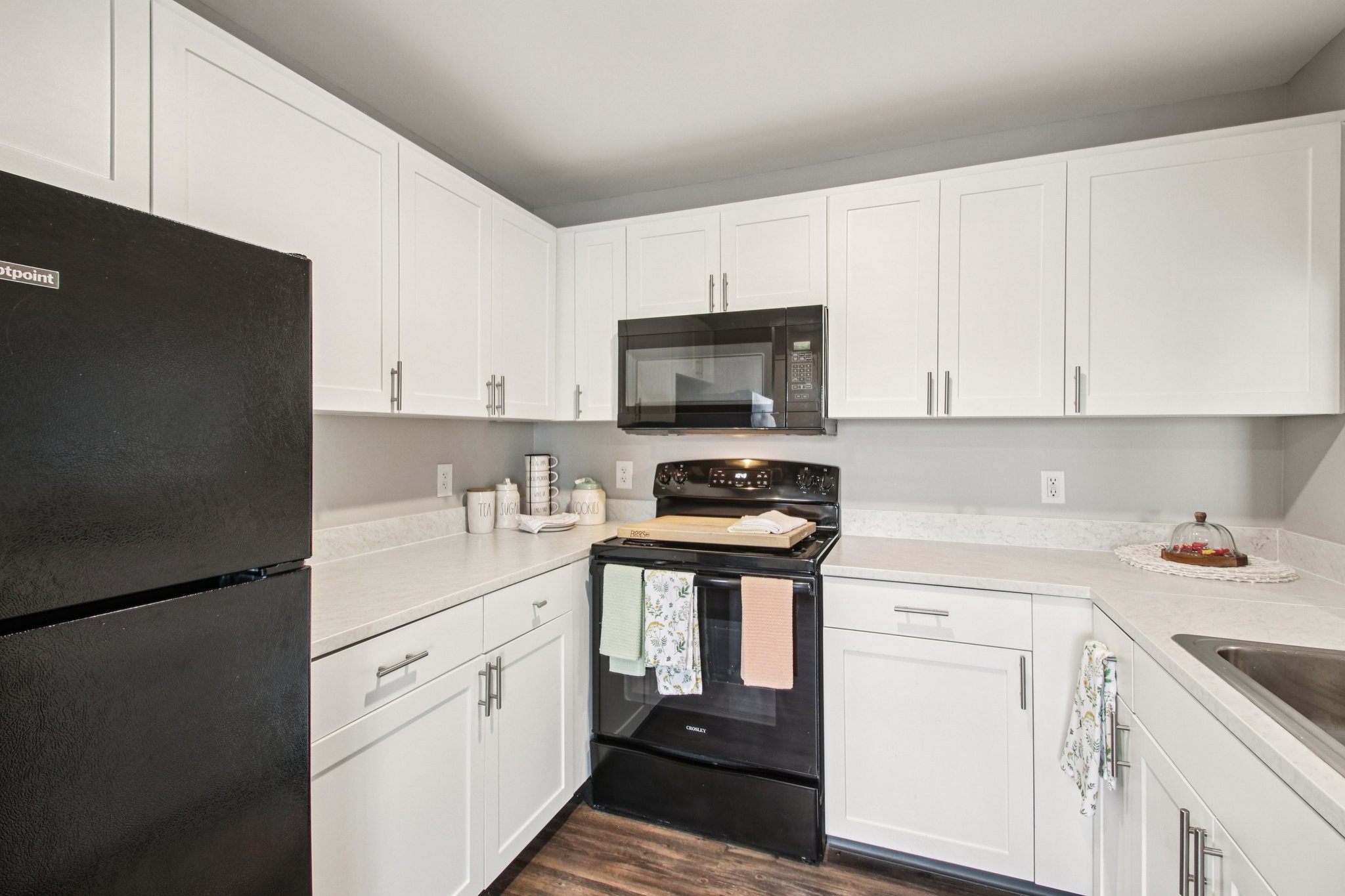 A black refrigerator is on the left in a kitchen with white cabinets.