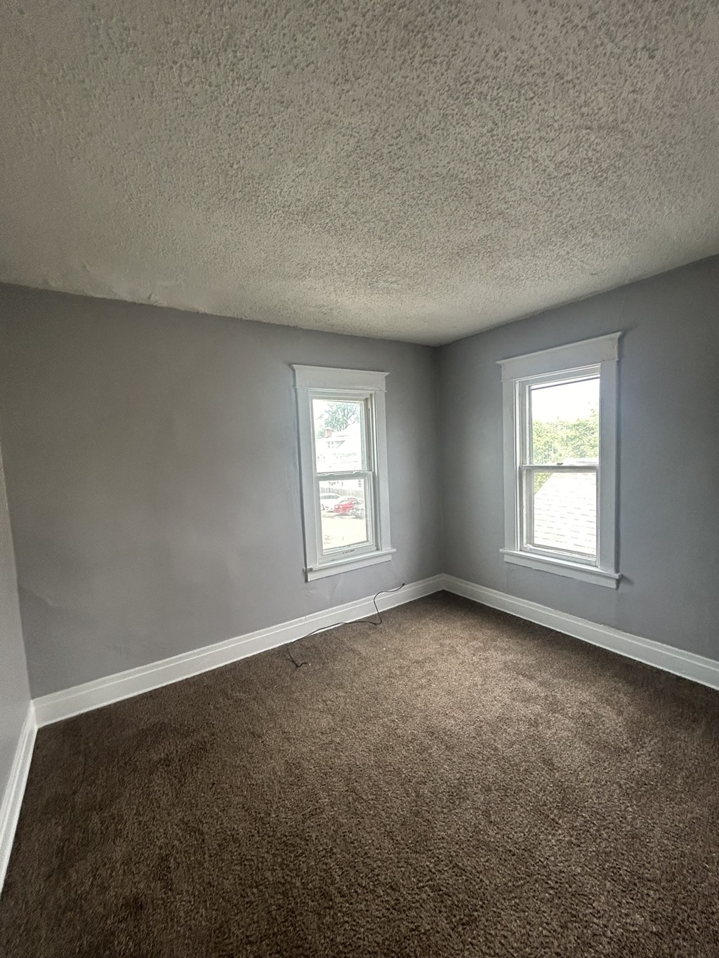 an empty room with gray walls and two windows