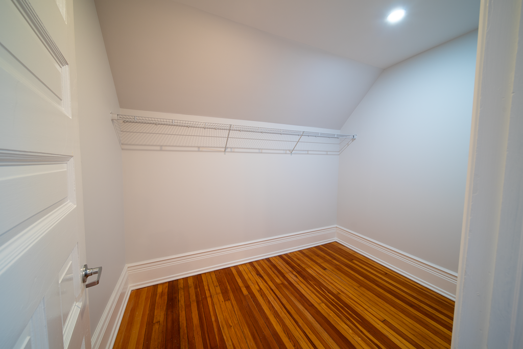 a bedroom with white walls and wood flooring and a closet