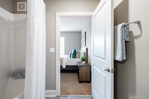 A white door is open to a bedroom with a bed and a nightstand.
