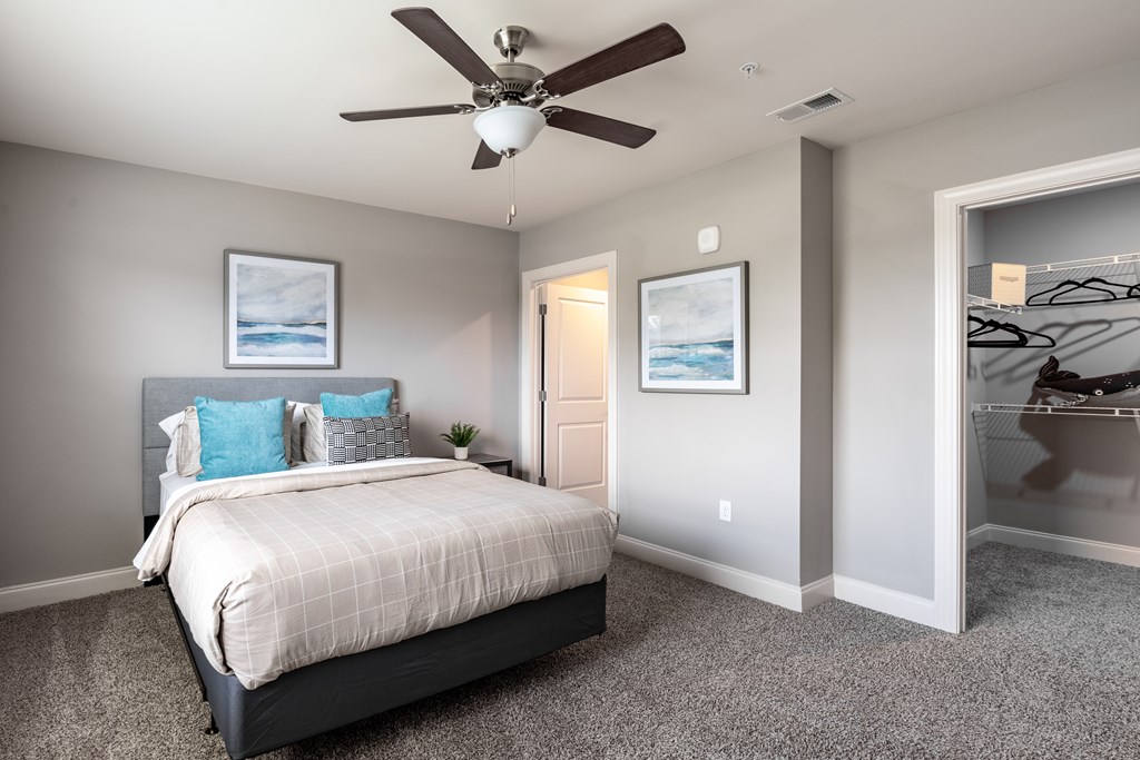 A bedroom with a bed, a ceiling fan, and two pictures on the wall.