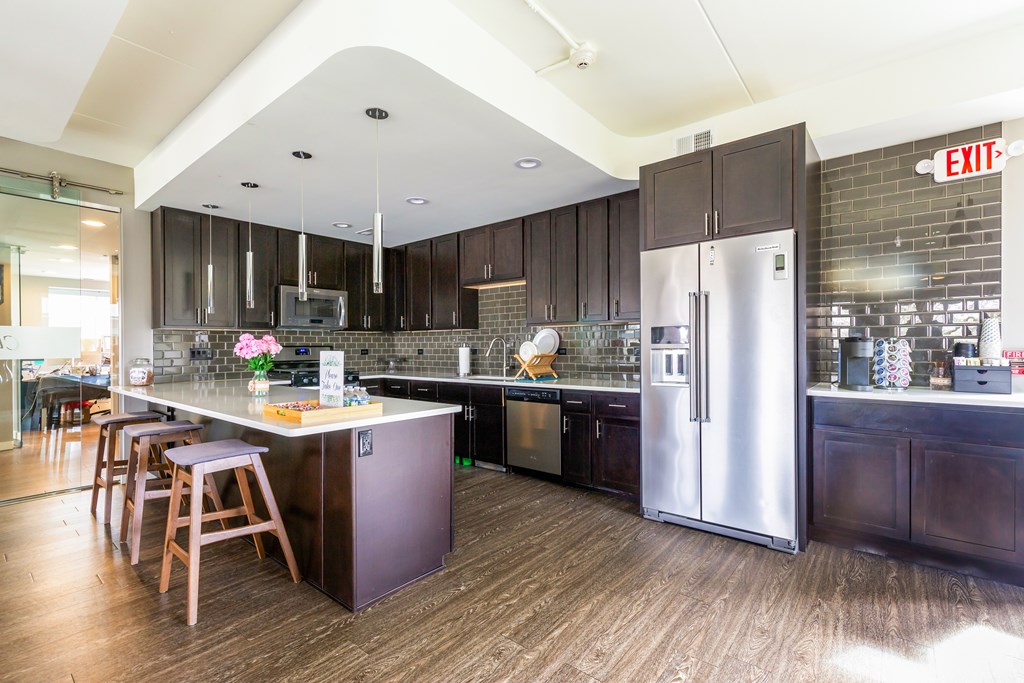 A kitchen with a refrigerator, stove, and bar stools.