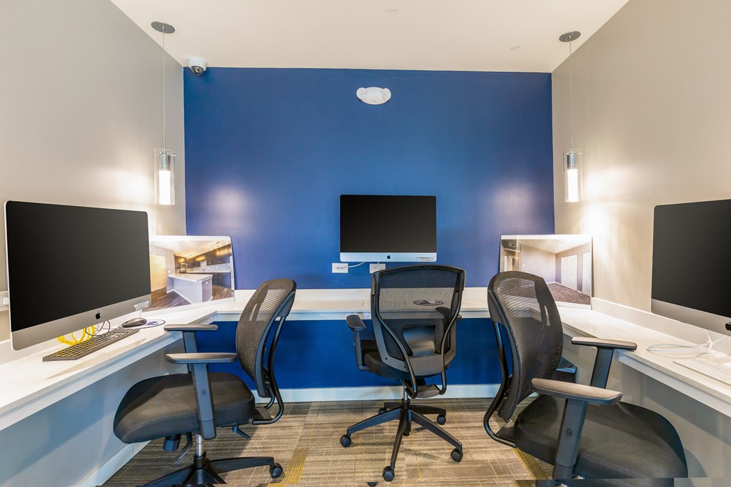 Three black chairs are positioned in front of two computer monitors in a room.