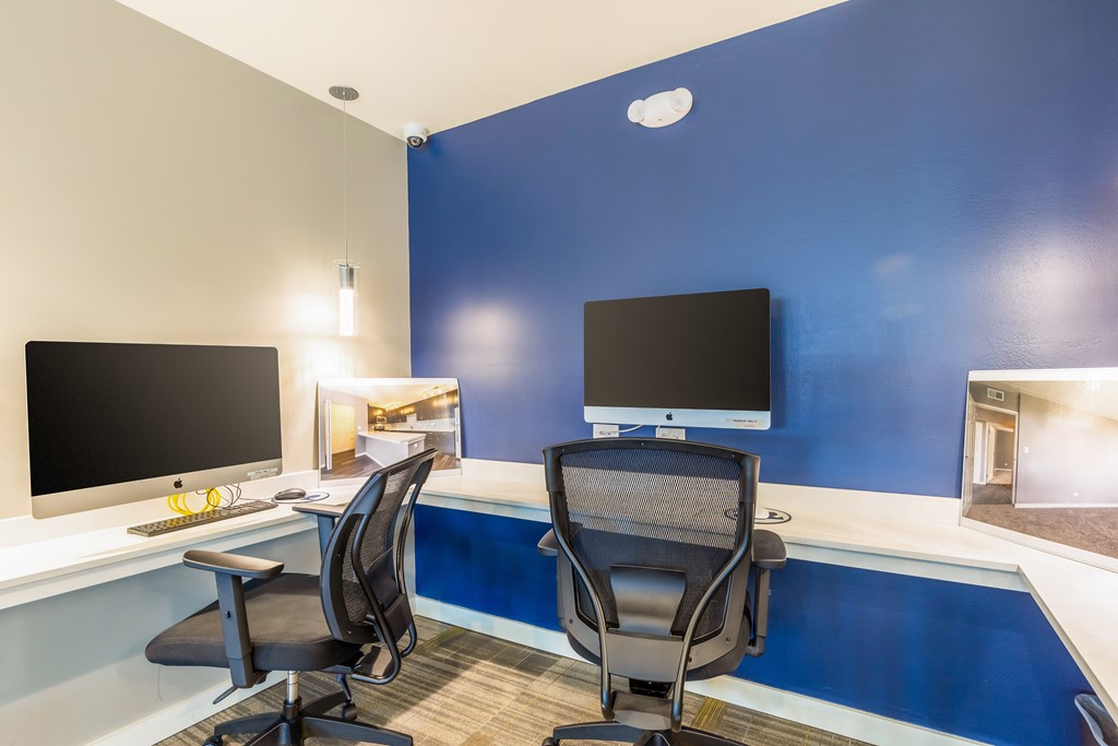 Two black computer monitors on a desk with two chairs.