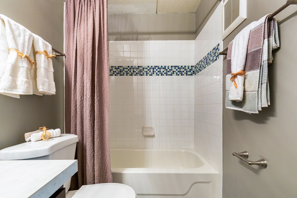 A bathroom with a white tub, a pink shower curtain, and a white towel hanging on the towel rack.