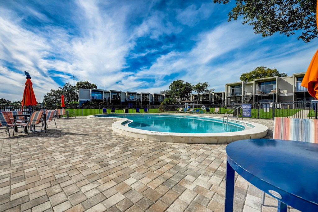 a resort style pool with chairs and umbrellas and apartments in the background
