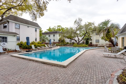 A swimming pool surrounded by a brick patio and lounge chairs.