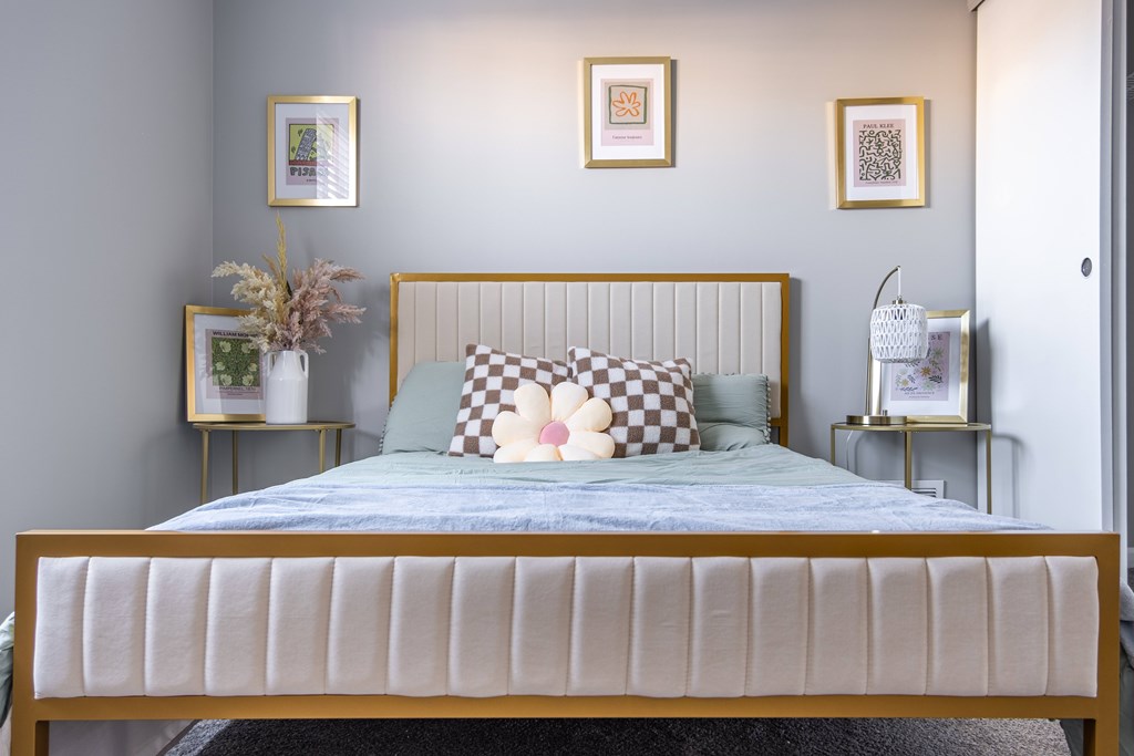 A bed with a white headboard and a blue bedspread with a checkered pillow in the middle at Centerpointe Apartments, Canandaigua, 14424