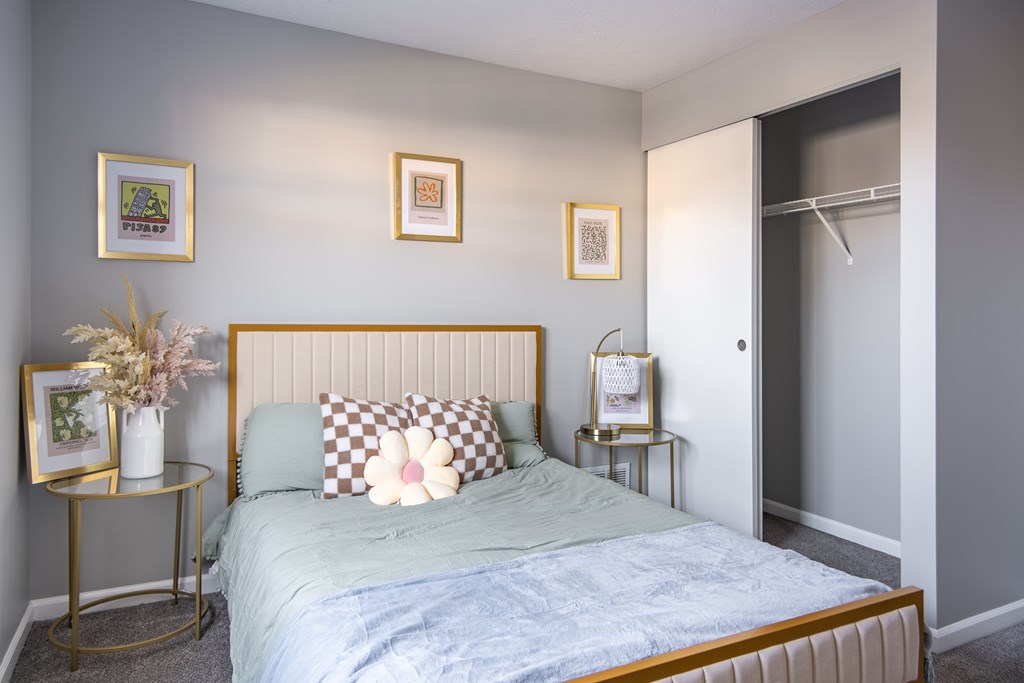 A bedroom with a bed, two side tables, and three framed pictures on the wall at Centerpointe Apartments, Canandaigua, New York