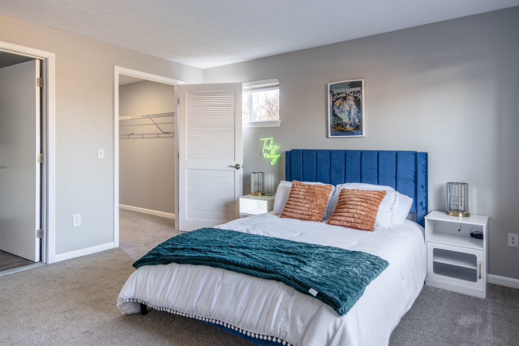 A bedroom with a bed, nightstand, and a painting on the wall at Centerpointe Apartments, Canandaigua, NY
