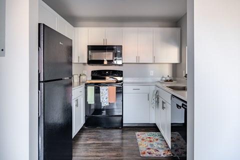 A black fridge and microwave in a kitchen with white cabinets.