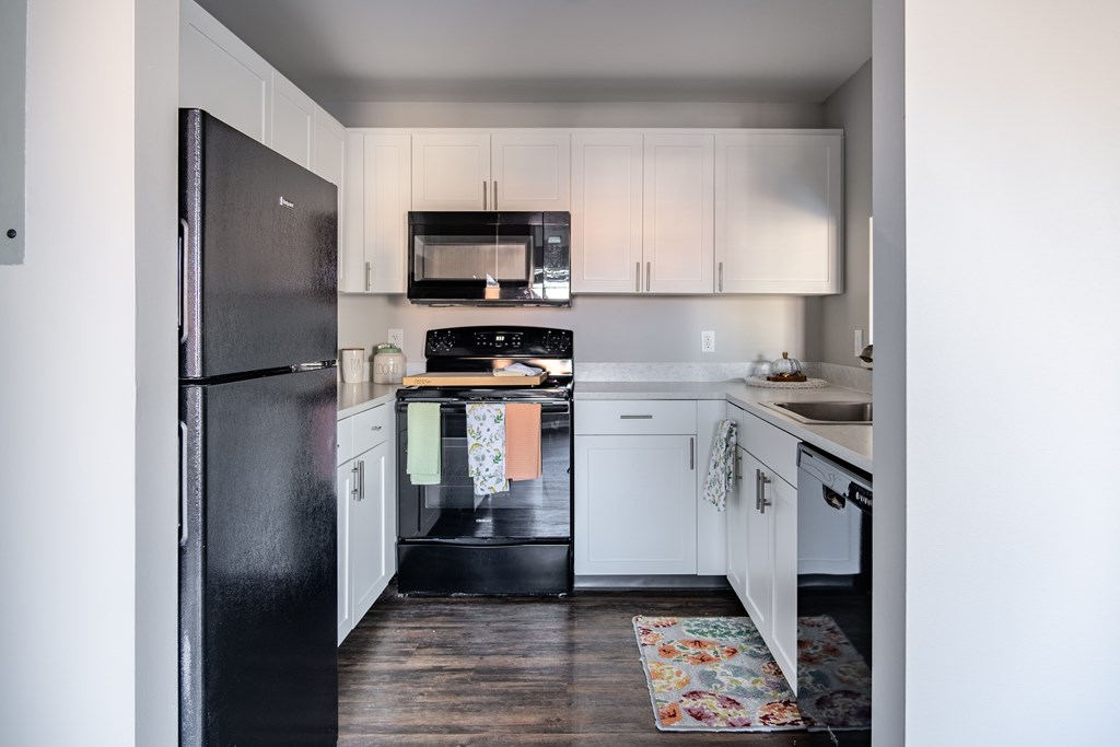 A black fridge and microwave in a kitchen with white cabinets.