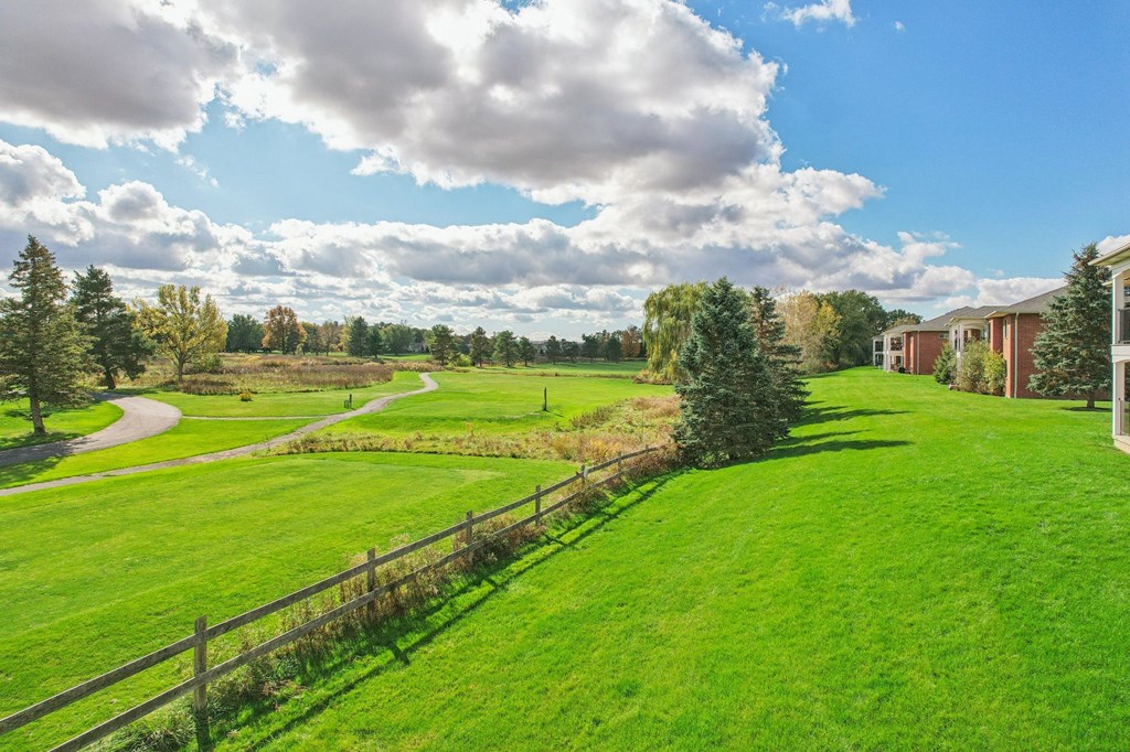 A grassy field with a fence and trees in the distance.