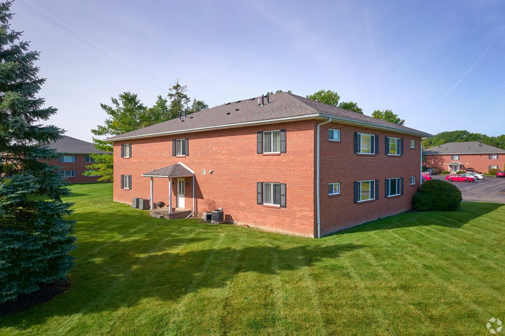a red brick house with a green lawn and a tree at Centerpointe Apartments, Canandaigua, New York