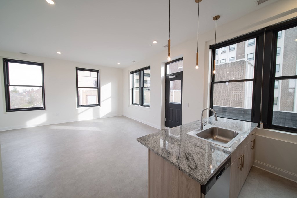 an empty living room and kitchen with a sink and windows