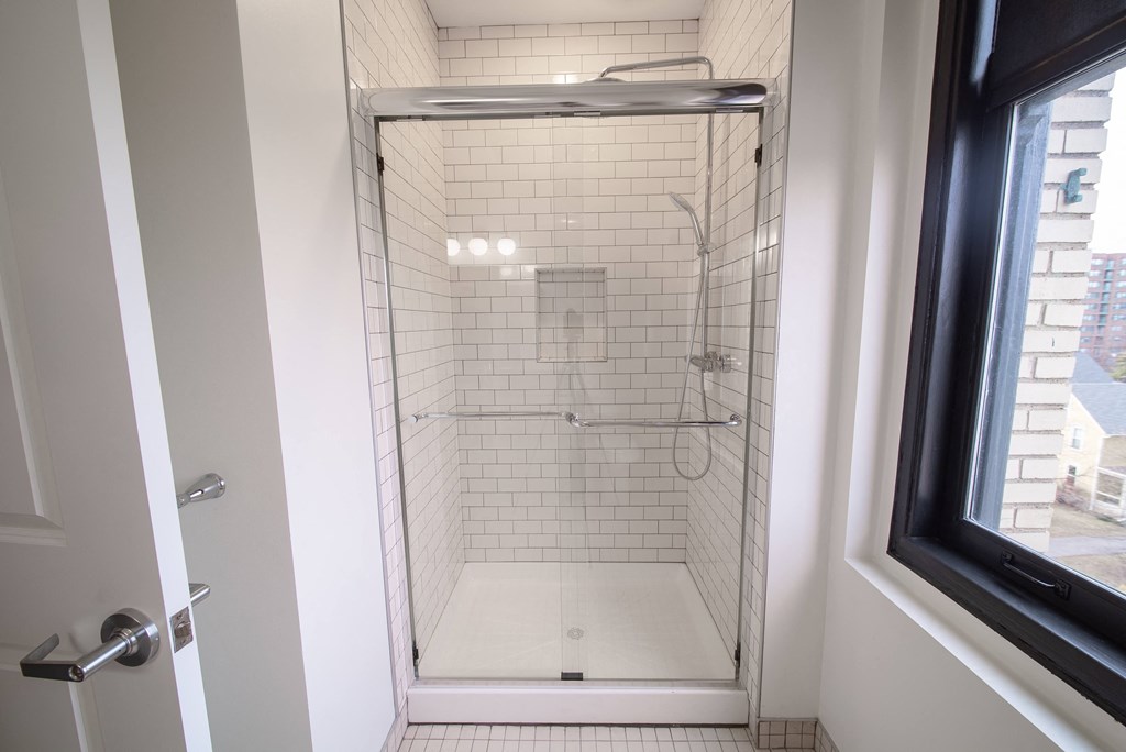 a small shower with white tile and a window