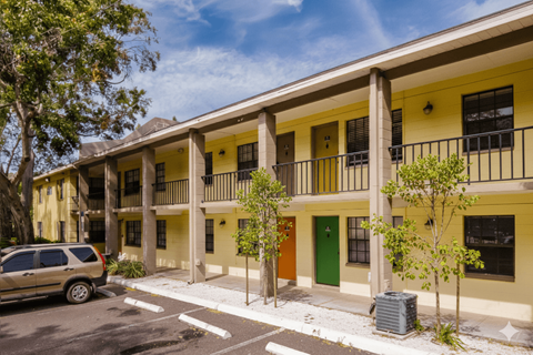 A yellow building with a green door and a tree in front of it.