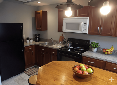 A kitchen with a black refrigerator, wooden cabinets, a black stove, and a wooden table with a bowl of fruit on it.