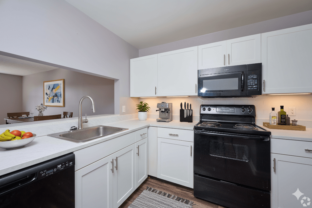 A modern kitchen with white cabinets and black appliances.