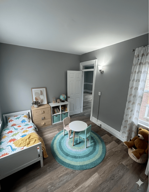 A child's bedroom with a bed, dresser, chair, and teddy bear.