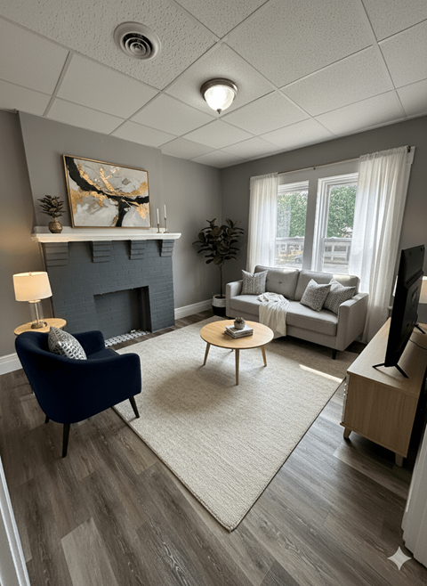 A living room with a blue armchair, a grey couch, a fireplace, and a painting on the wall.