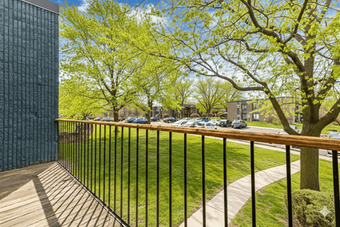A balcony with a black railing and a view of a green lawn and trees.