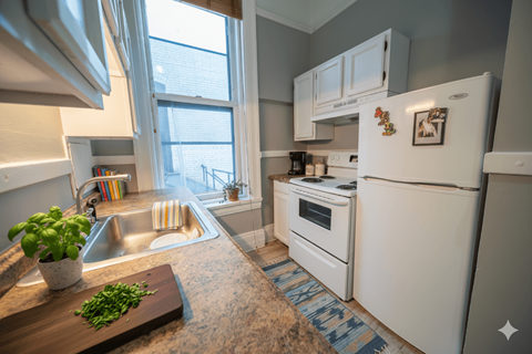 A kitchen with a white refrigerator and a wooden cutting board with green herbs on it.