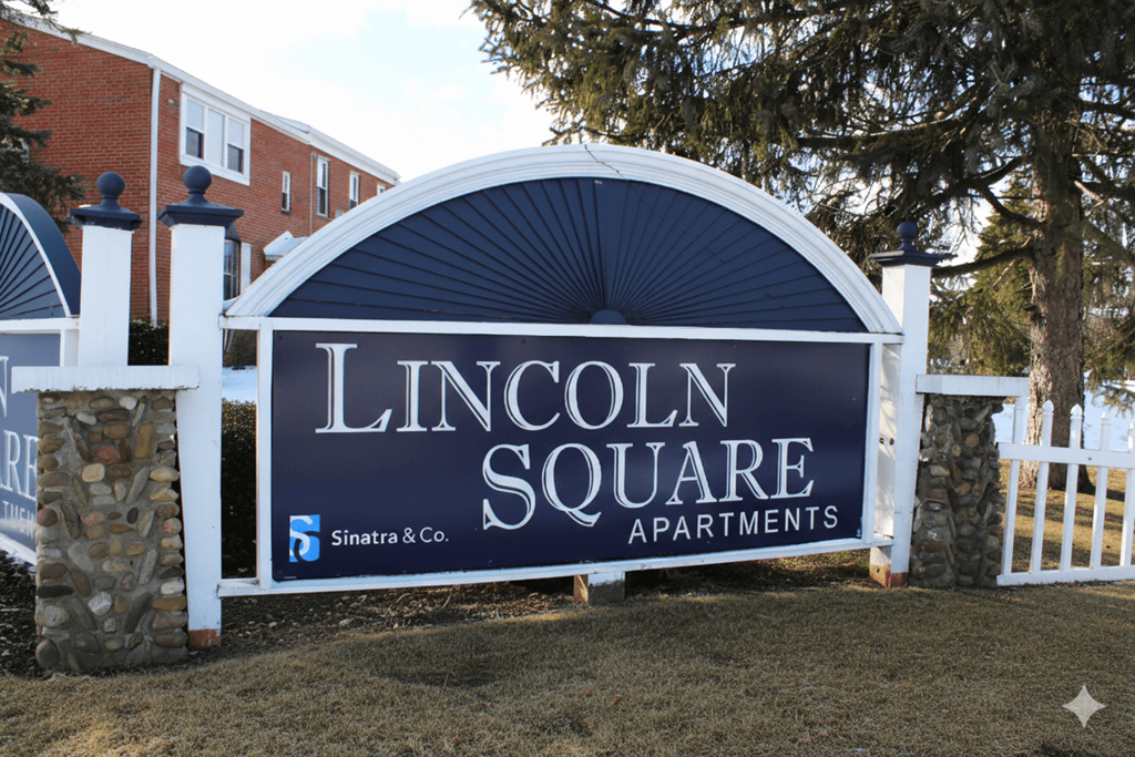 A sign for Lincoln Square Apartments is displayed in front of a white fence.