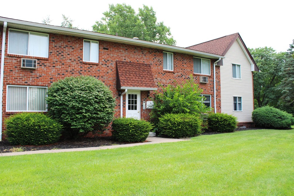 a red brick house with white siding and a green lawn at Highview Manor Apartments, Fairport, 14450
