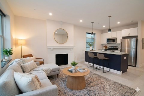 A modern living room with a fireplace and a kitchen area in the background.