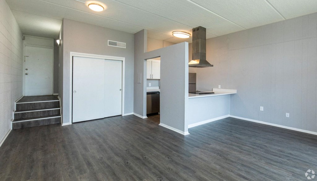 an empty living room with a kitchen in the background