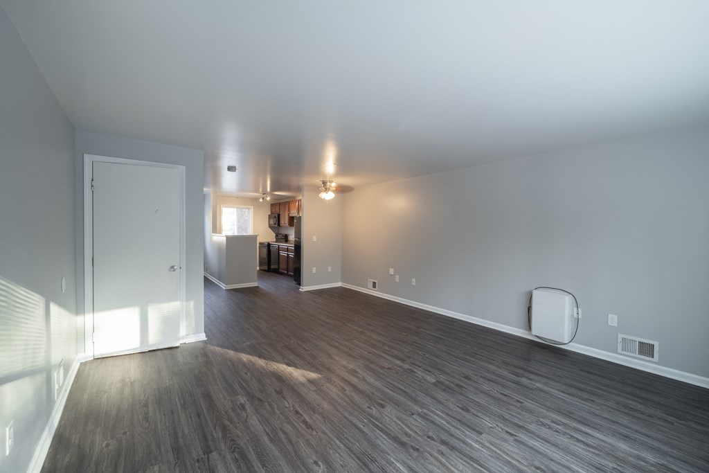 an empty living room with wood flooring and a door into a kitchen at Willowbrooke Apartments, Brockport, NY