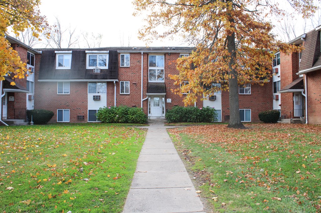 an apartment building with a sidewalk and a tree in front of it at Willowbrooke Apartments, Brockport, 14420