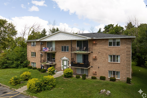 A large brick apartment building with a balcony and a small garden in front.