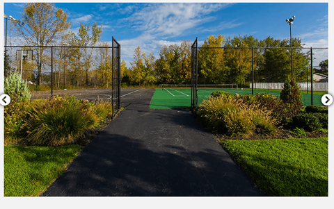 A tennis court is surrounded by a fence and a pathway.