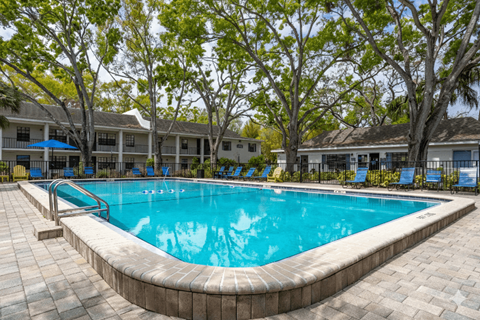 A swimming pool surrounded by trees and chairs.