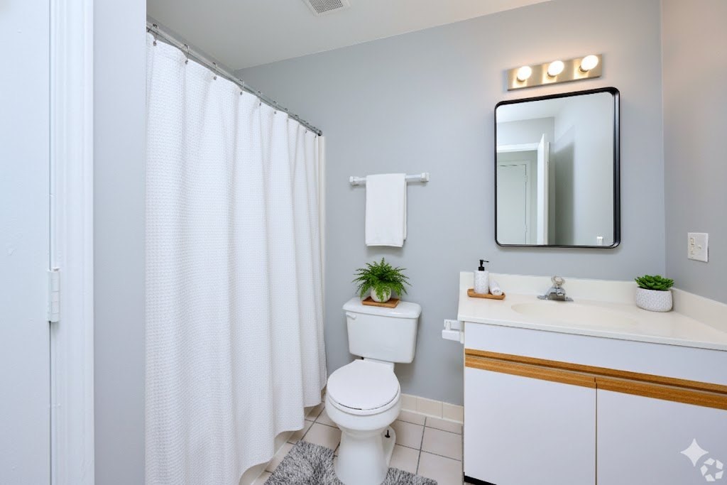 A white toilet sits in a bathroom with a white shower curtain.