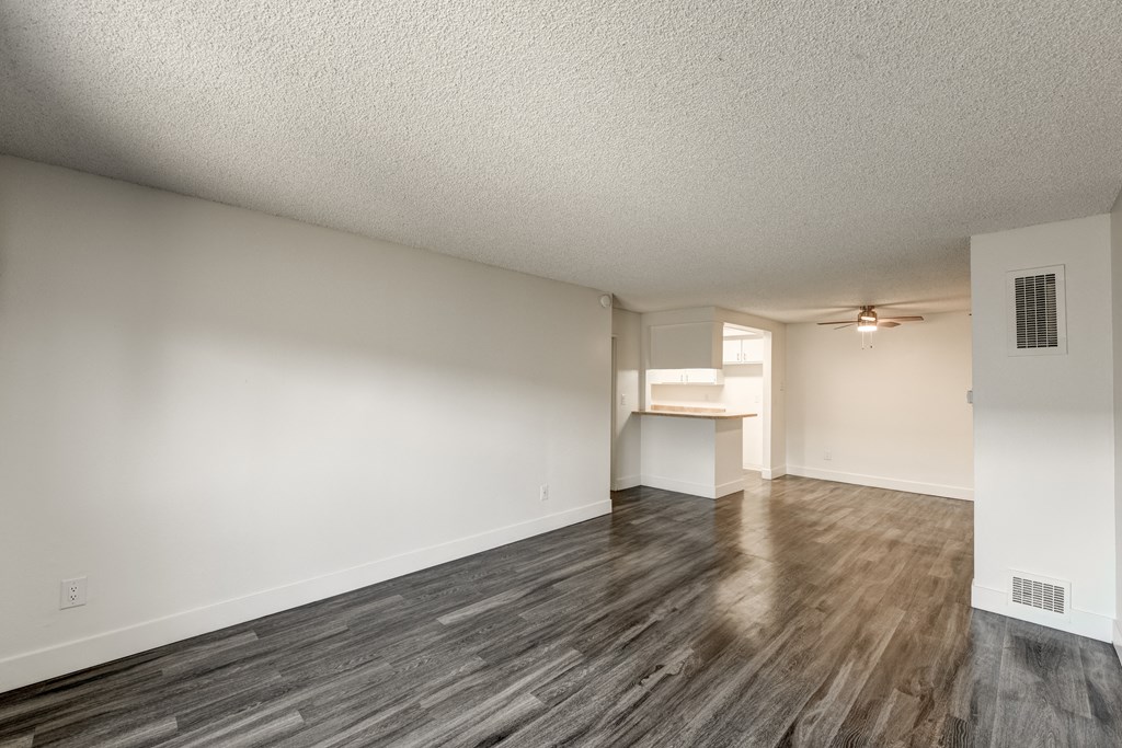 an empty living room and kitchen with wood flooring and a ceiling fan