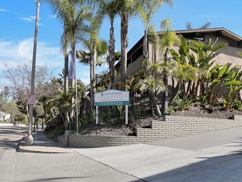 A sign for "Idylwood" stands in front of a building with a brick wall and palm trees.