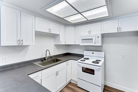 A white kitchen with a stove, sink, and cabinets.