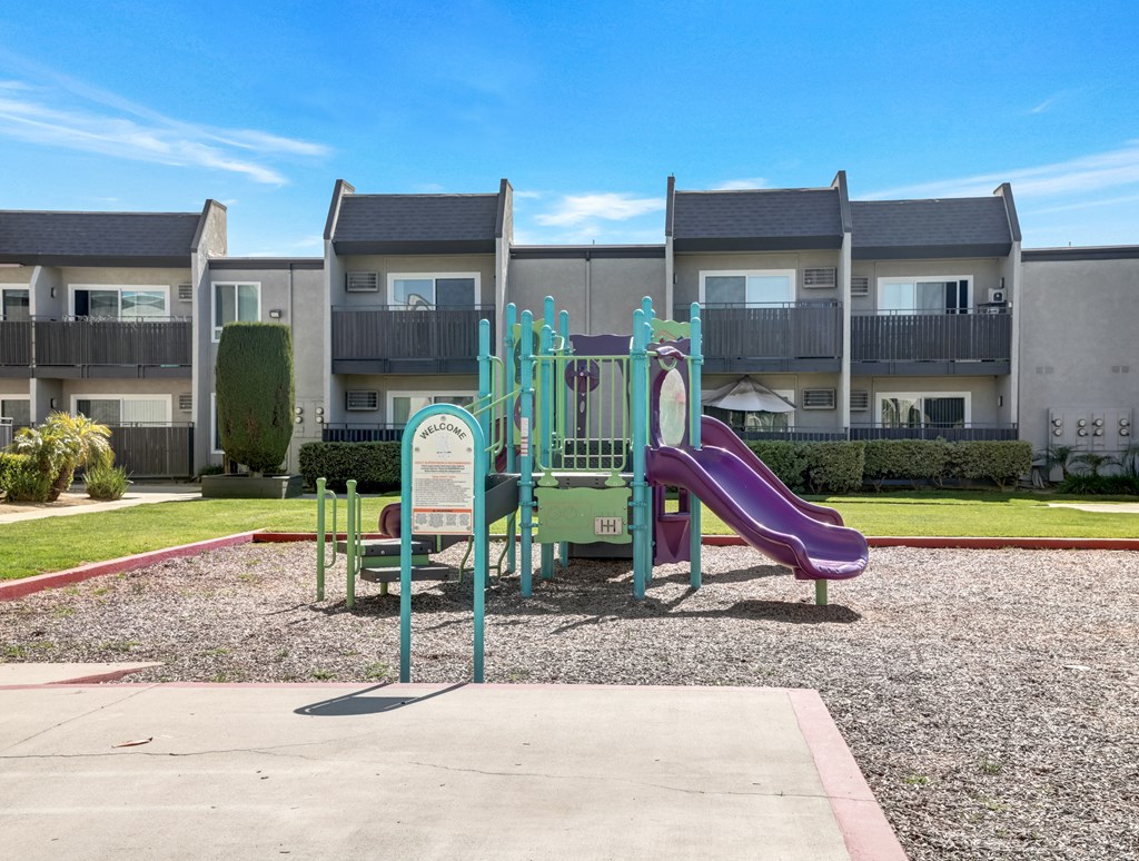 A playground with a purple slide and a green and white sign.