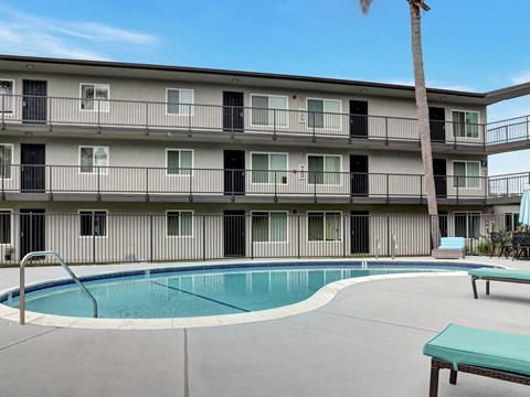 A pool is surrounded by a concrete patio and a building with balconies.