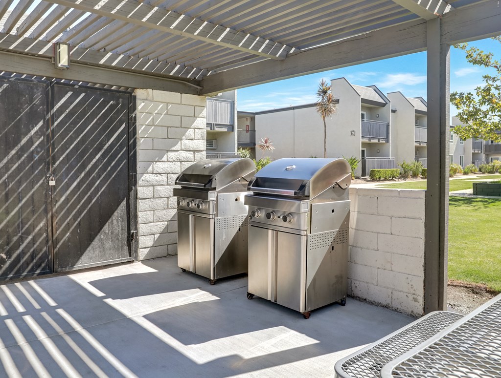 Two stainless steel barbecues are placed under a covered patio area.