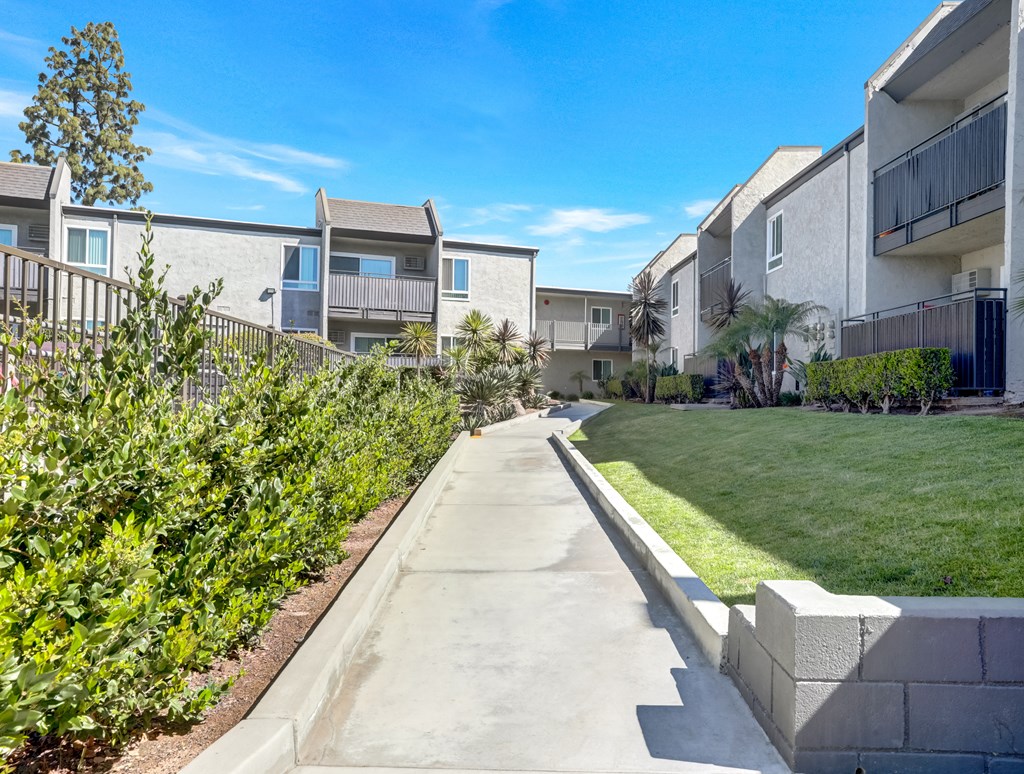 A concrete pathway leads through a well-manicured grassy area in front of apartment buildings.