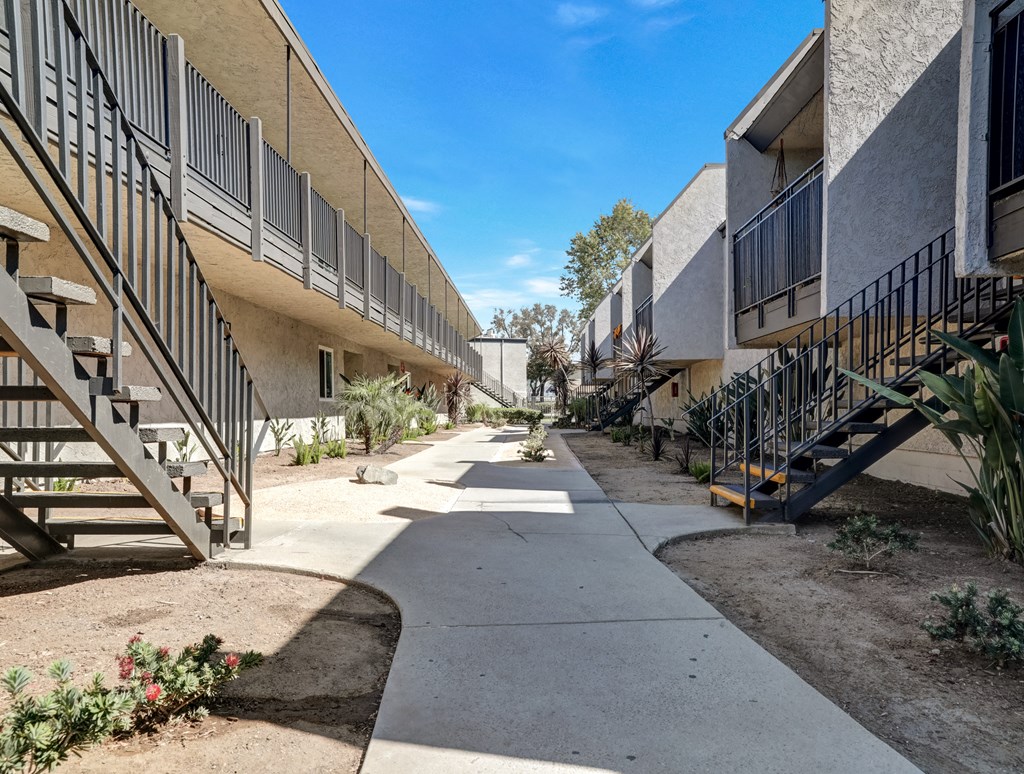 A concrete pathway leads between apartment buildings with metal staircases on either side.