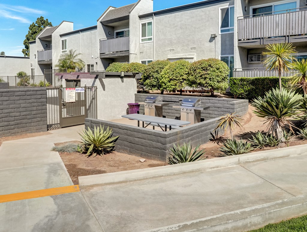 A concrete patio with a brick wall and a small garden in front of apartment buildings.