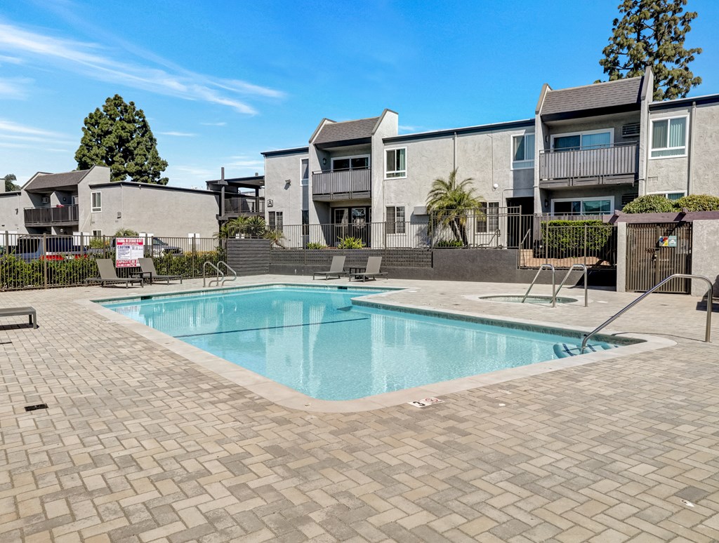 A swimming pool surrounded by a brick patio and apartment buildings.
