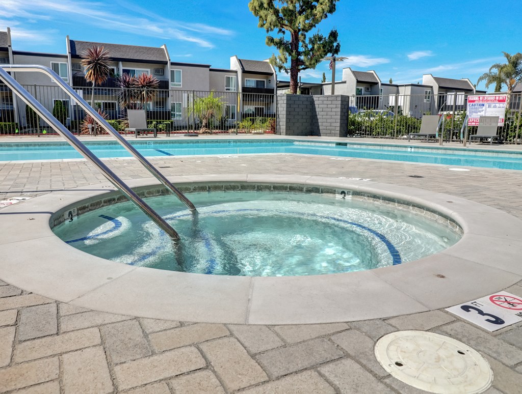 A hot tub in the middle of a brick patio with a pool in the background.