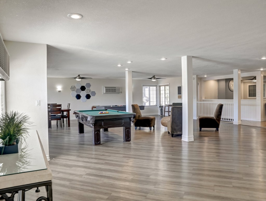 A pool table is in the middle of a room with a glass table and chairs.